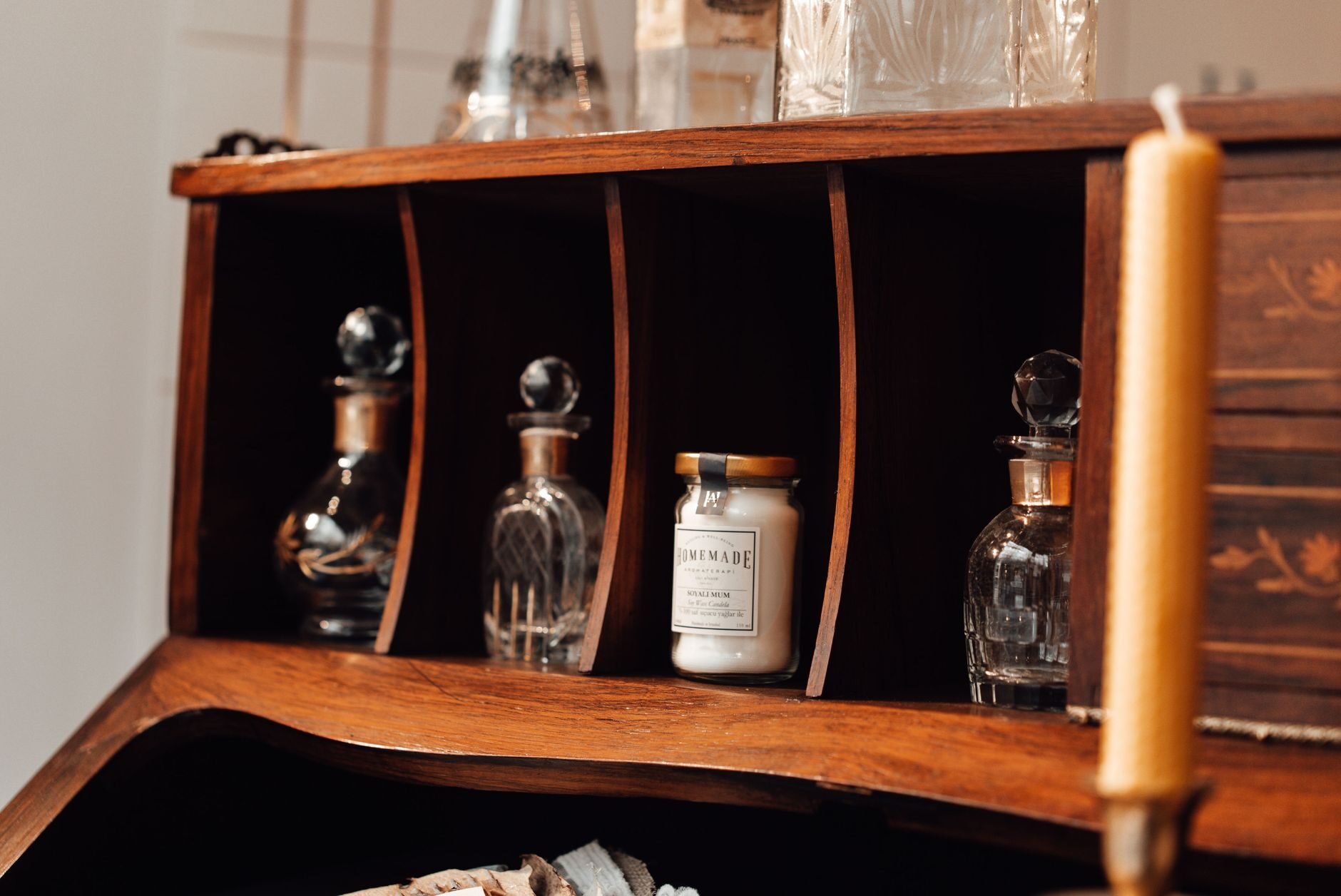 Curated glass bottles and a honey jar on a warm walnut secretary desk