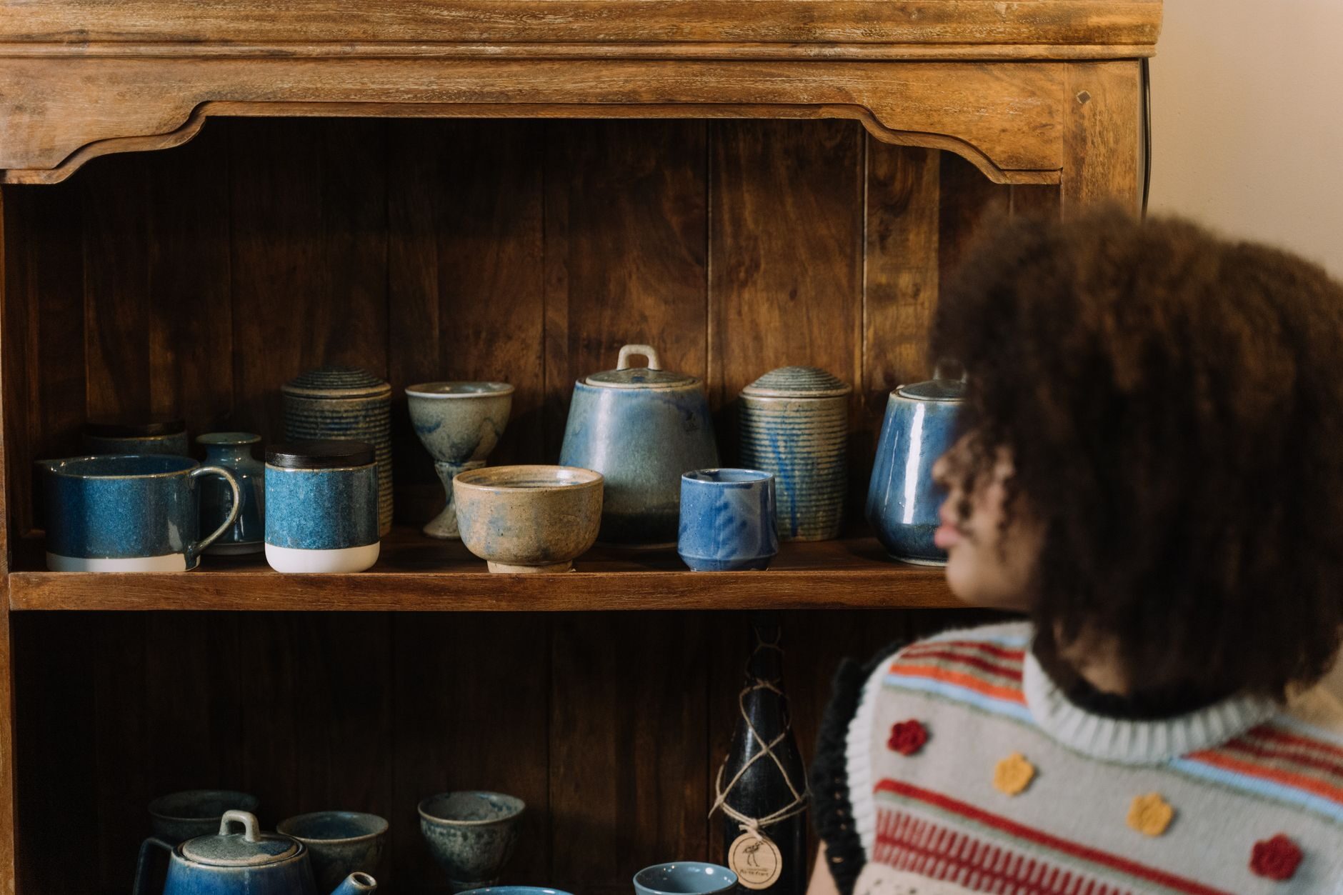 A customer browsing artisan blue stoneware on a dark antique wood hutch