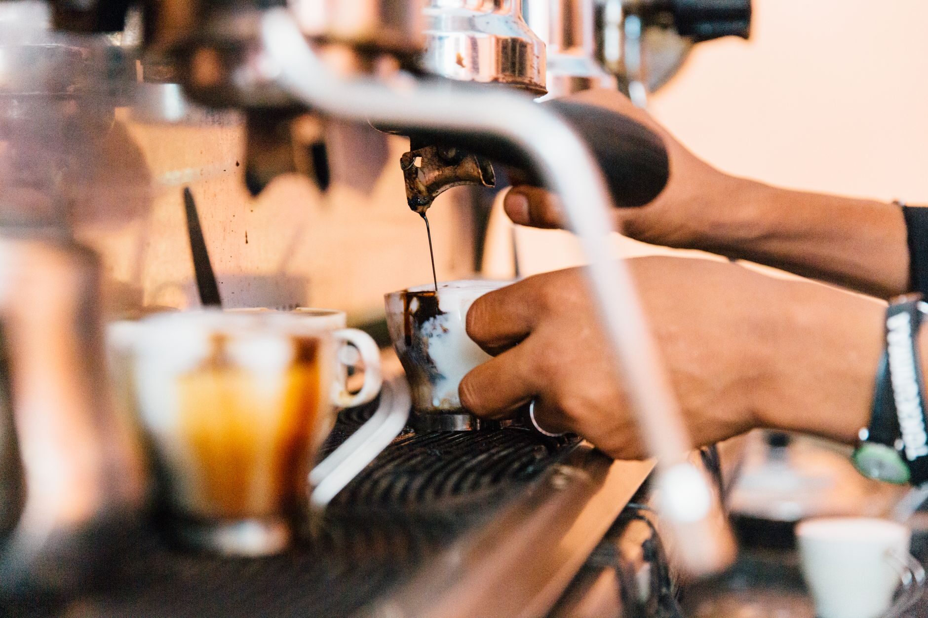 Barista's hands pulling a shot of espresso at the machine in warm light