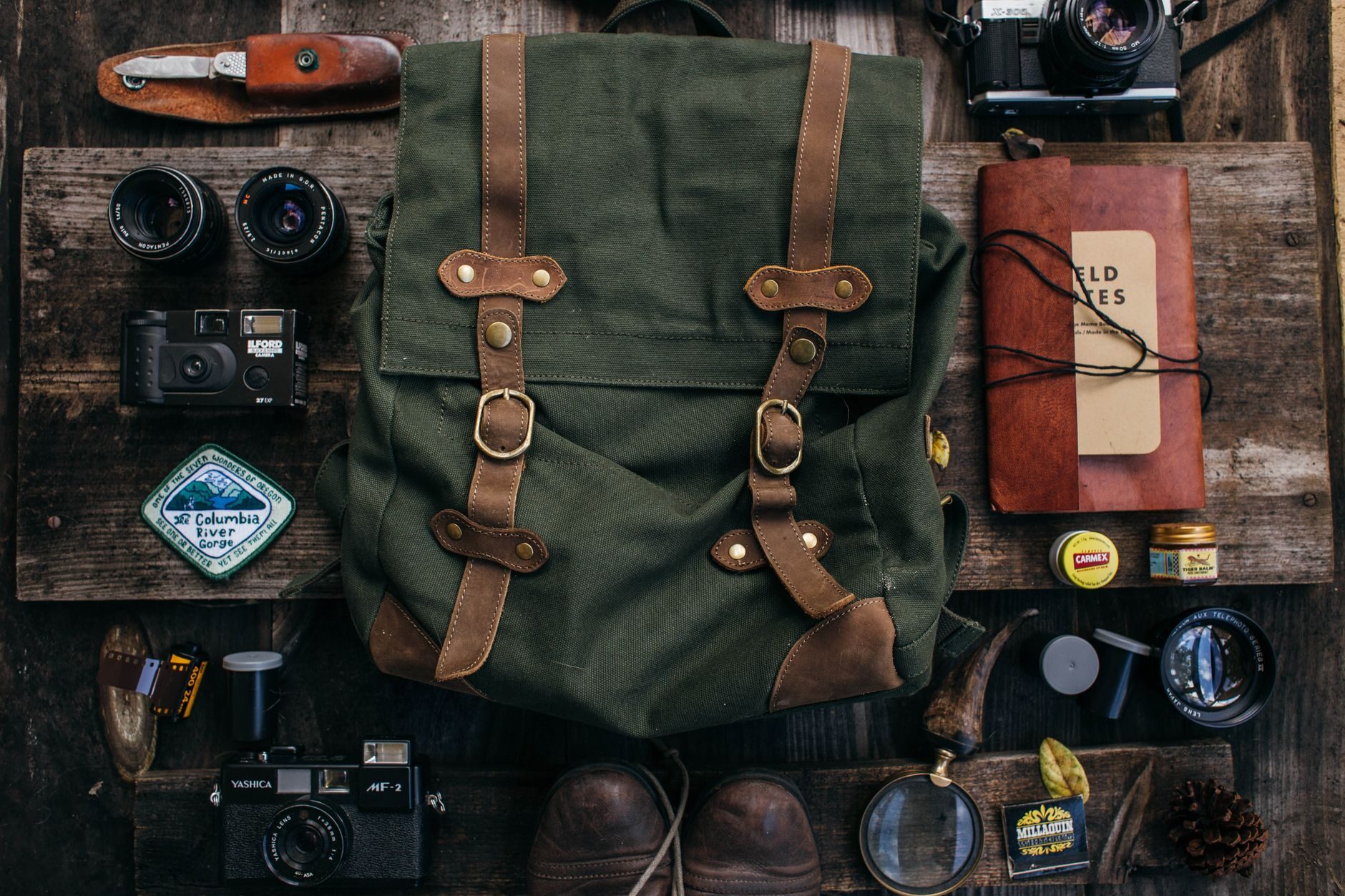 Olive canvas and leather backpack with field gear laid out on dark wood