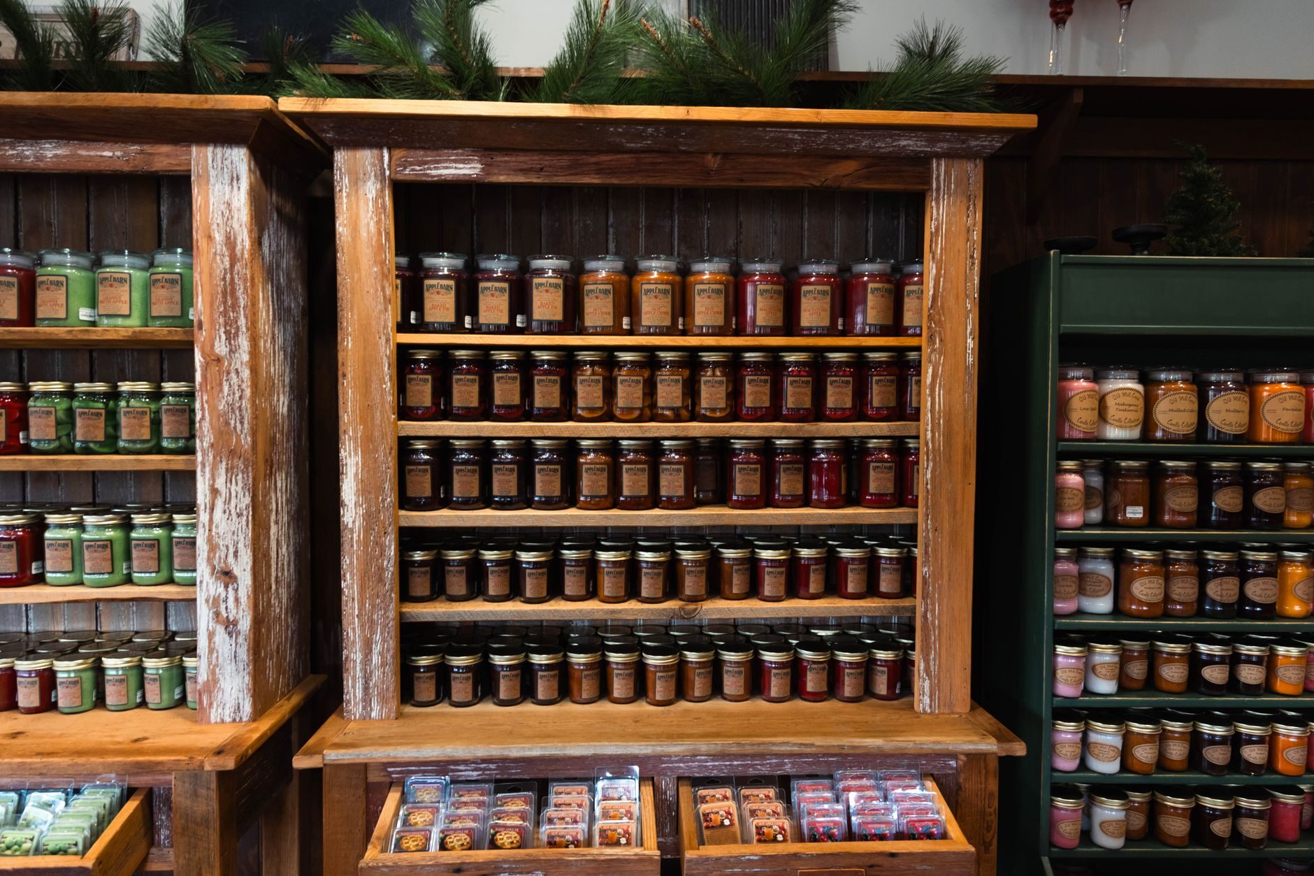 Rustic wood shelves lined with labeled jars of preserves and pine boughs